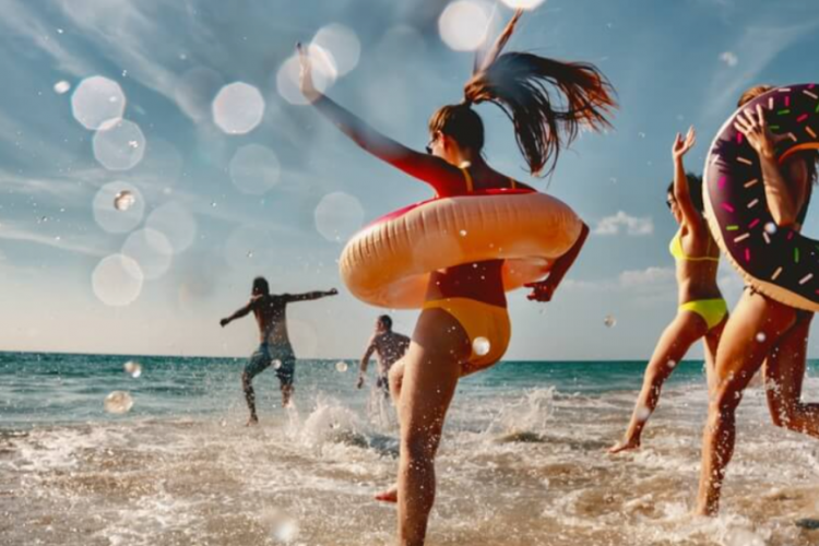 a group of people jumping in the ocean. a few of them are carrying pool floats.
