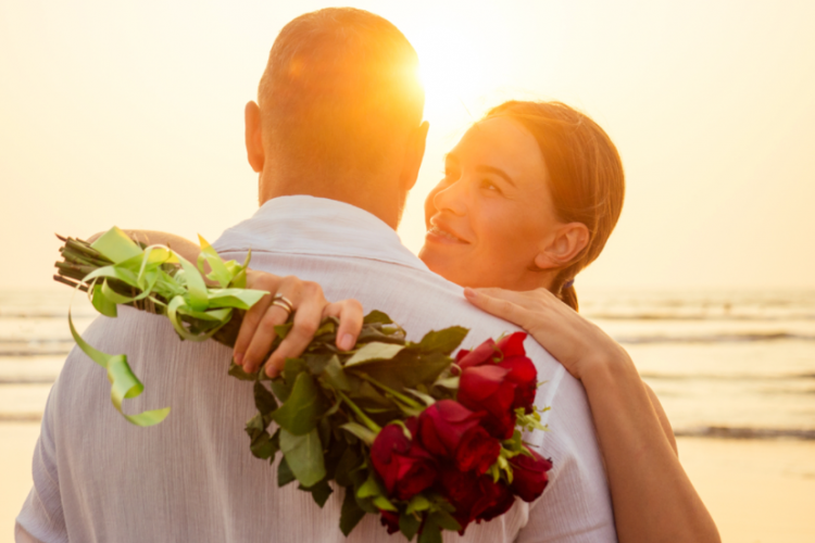 couple embracing on the beach, woman holding a bouquet of roses